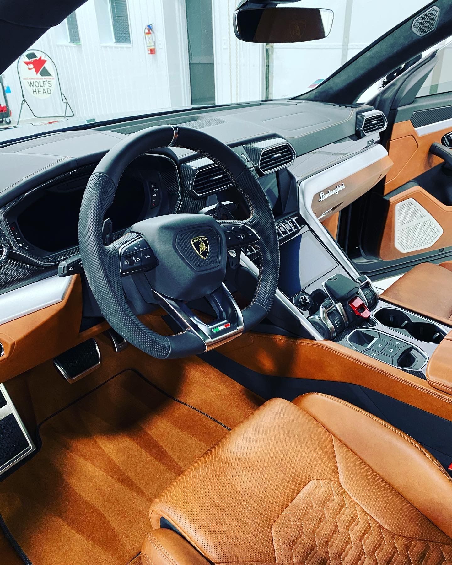 Luxury sports car interior with tan leather seats, black steering wheel, and carbon fiber trim