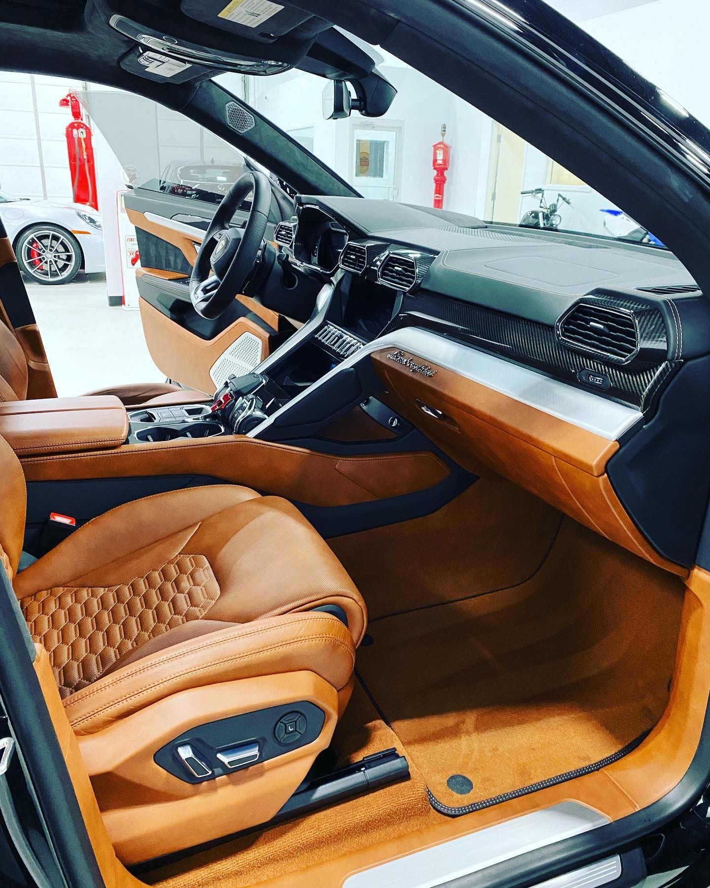 Luxury car interior with tan leather seats, wood trim, and a black dashboard viewed from the open driver’s door