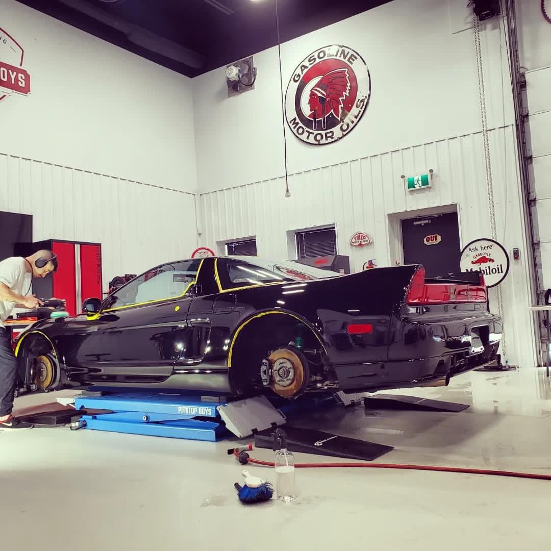 Black sports car on a lift in an auto shop, with mechanic working beside it.