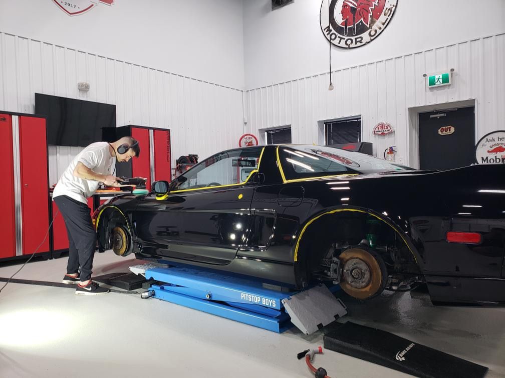 Mechanic working on a black car lifted on a blue alignment rack in an auto shop