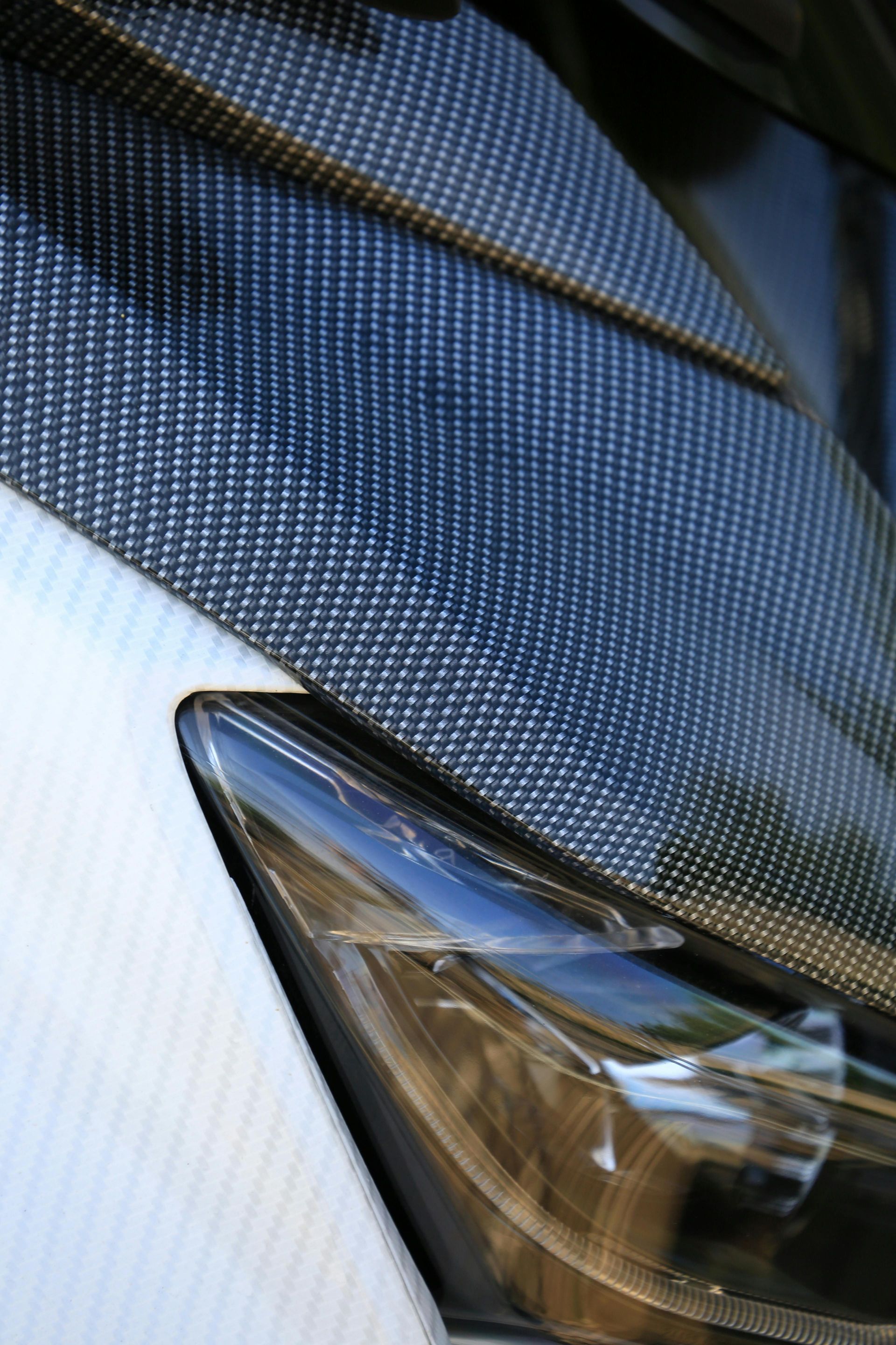 Close-up of a silver car headlight and blue carbon-fiber hood detail