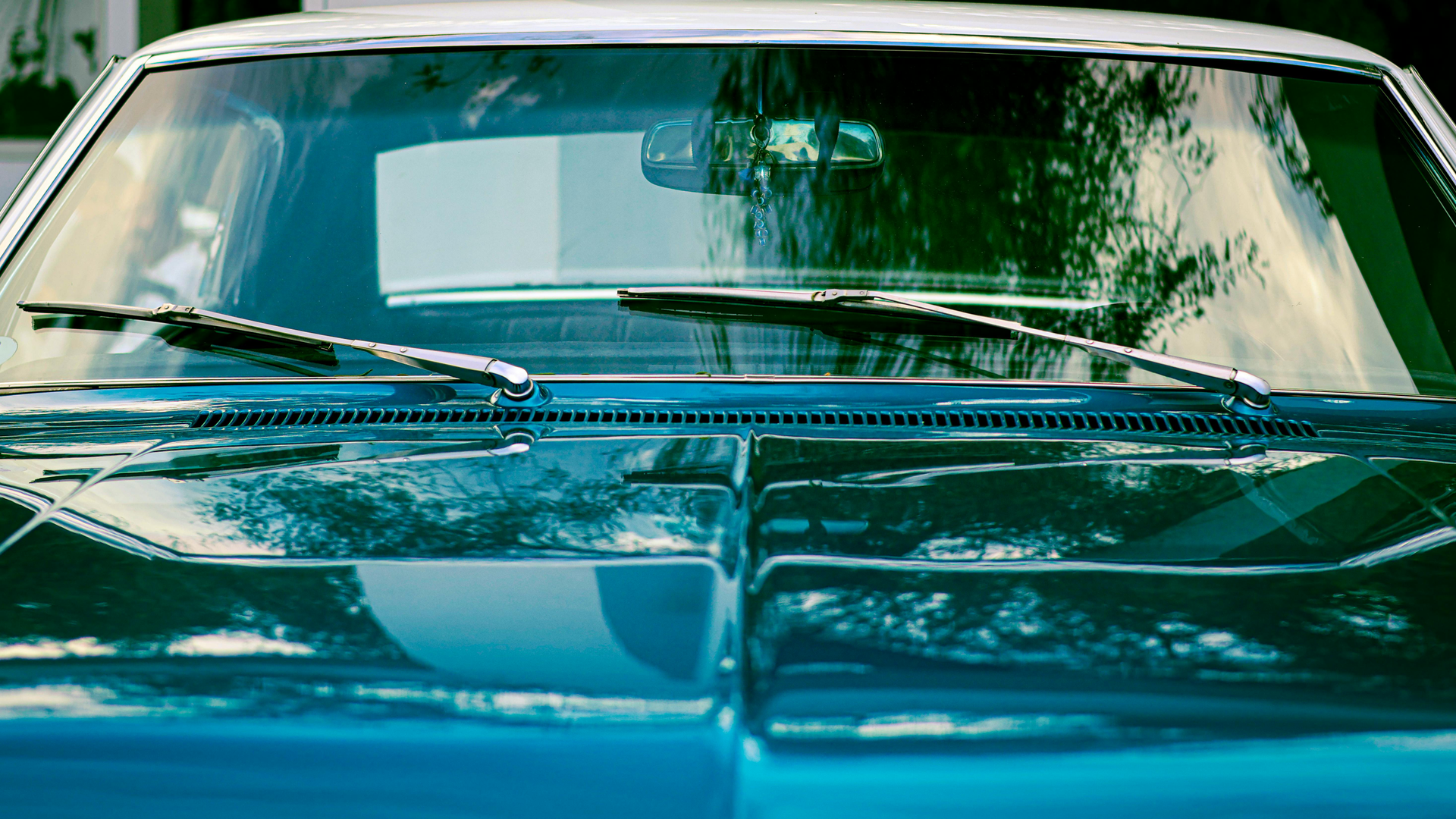 Front view of a teal classic car with windshield and reflections of trees on the hood