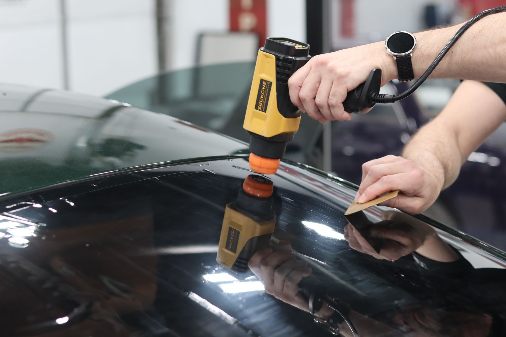 Person using a polishing tool on a black car windshield in a garage