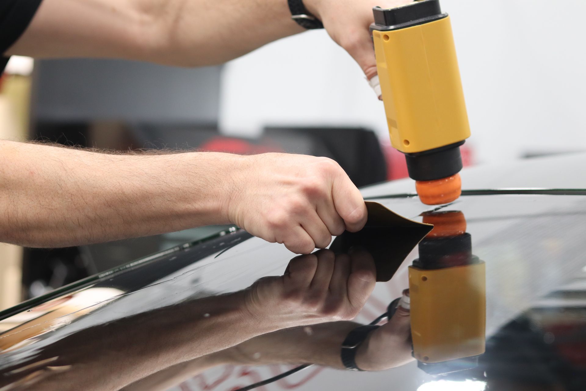 Hands using a yellow heat gun to apply tint film on a car window