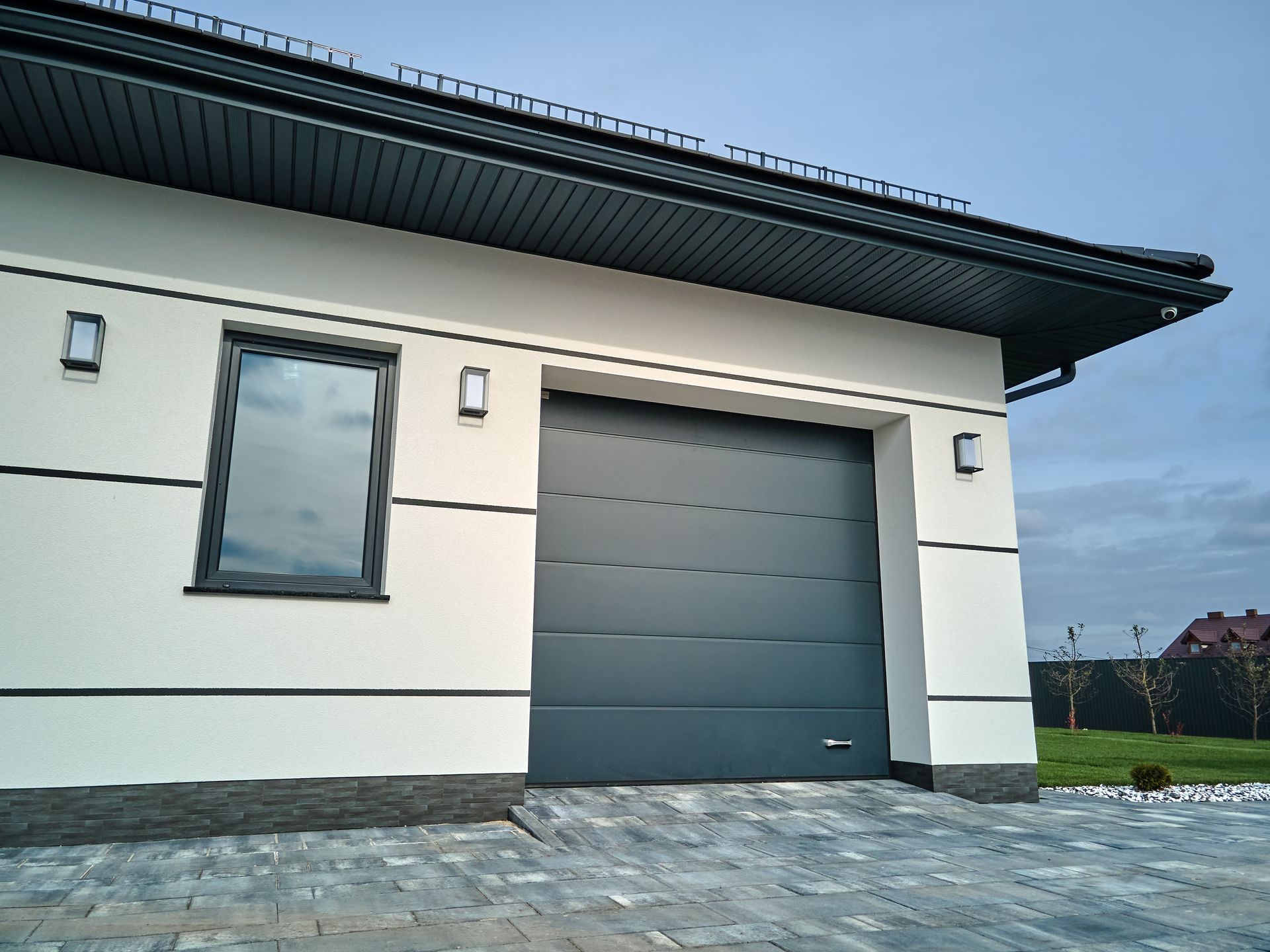 Modern white building exterior with a large gray garage door and stone driveway