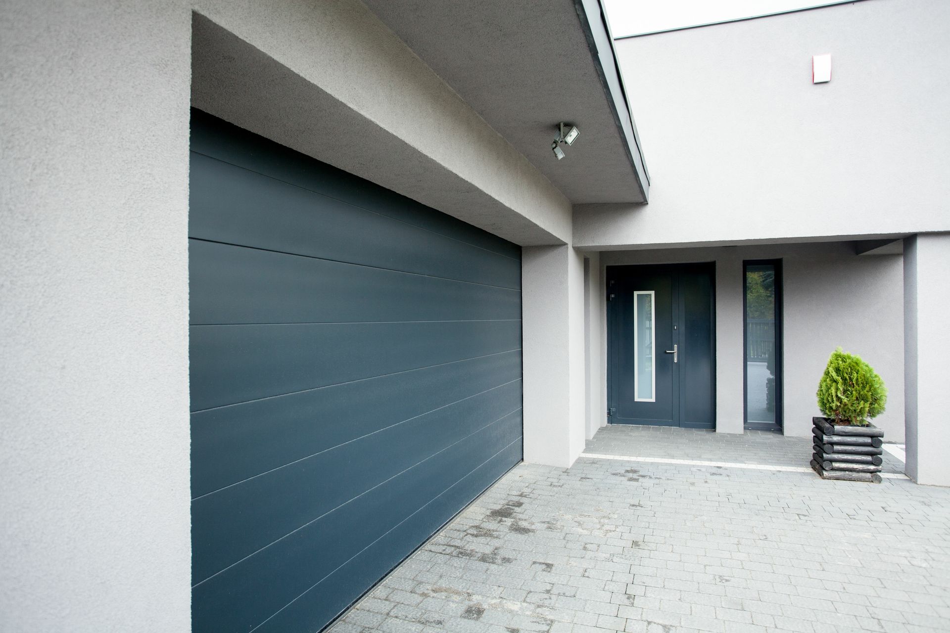 Modern gray house exterior with large garage door and front entryway with potted shrub