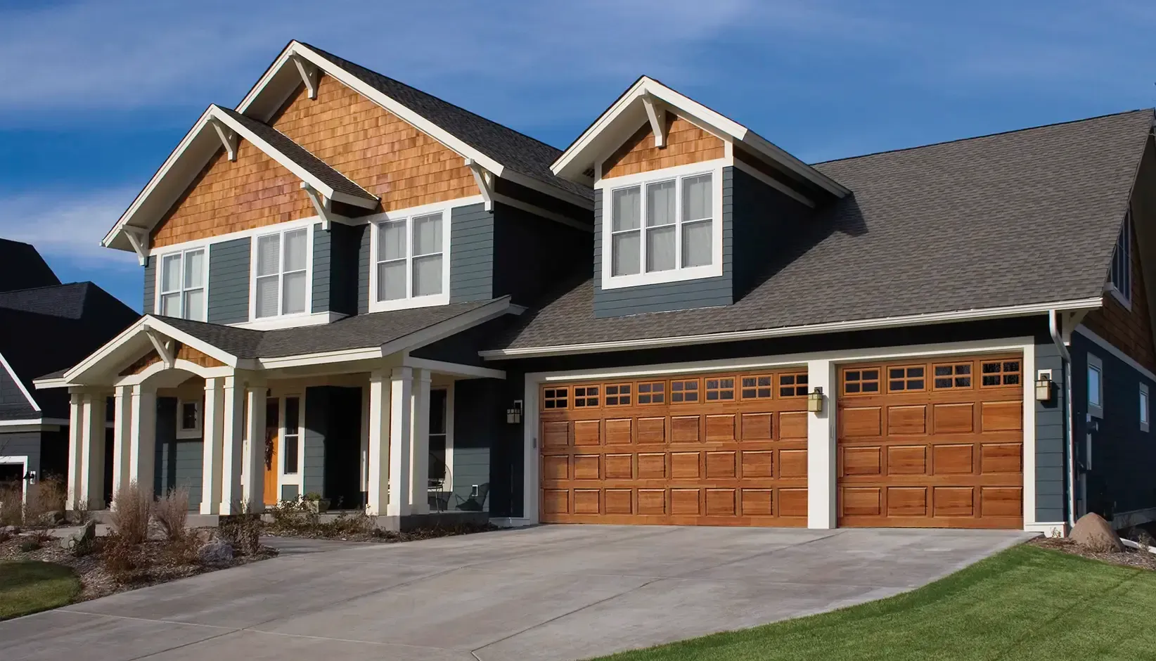 Suburban two-story house with gray siding, wood accents, and a three-car garage on a sunny day