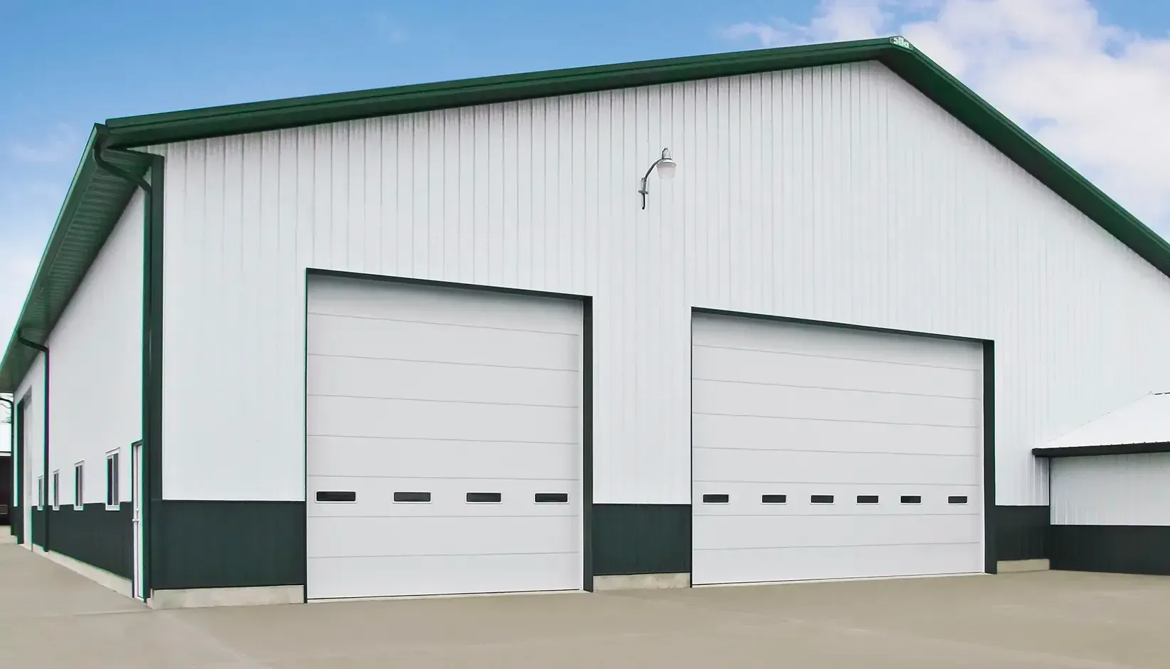 White industrial garage building with two large roll-up doors and green trim
