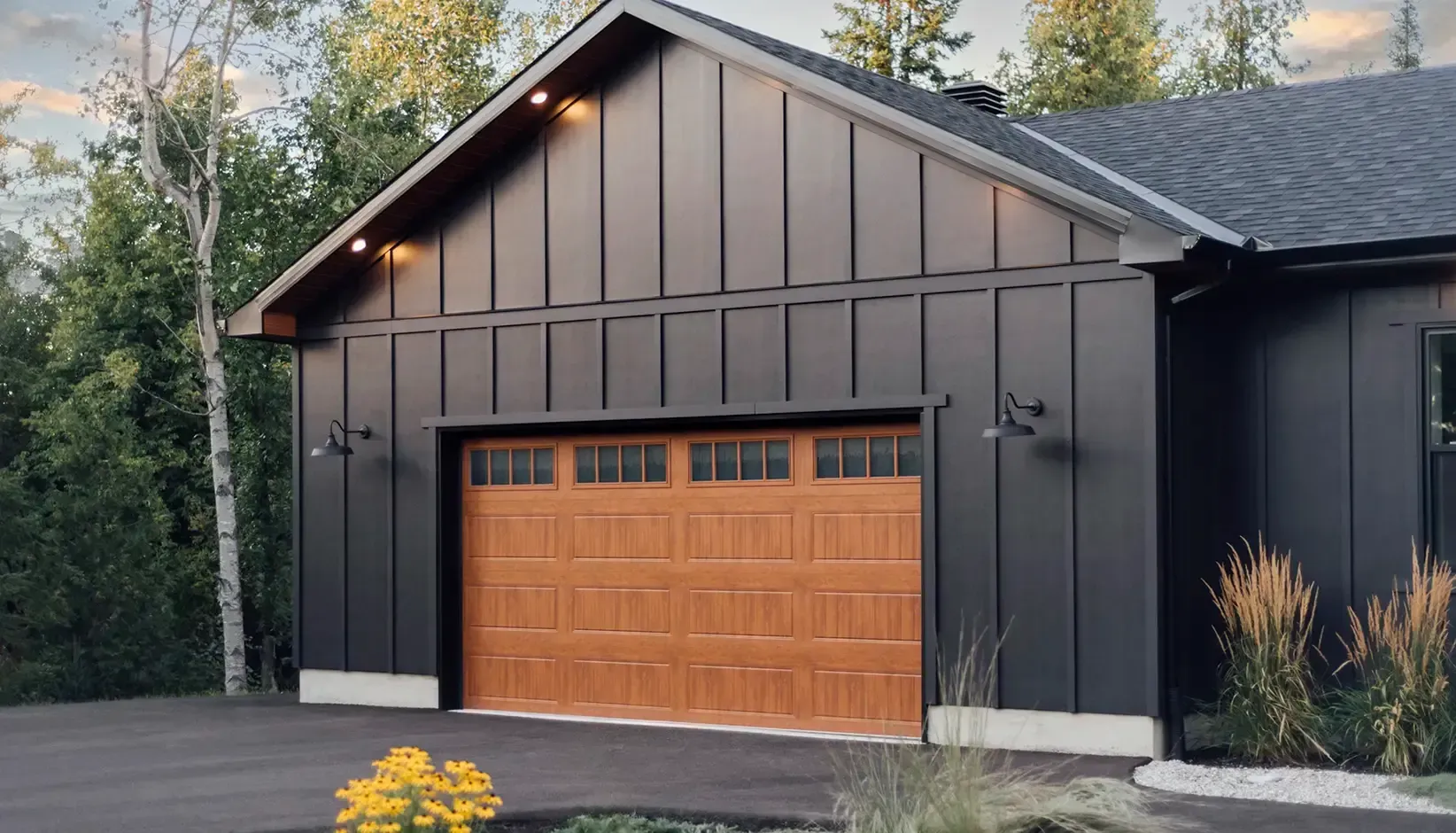 Modern dark-gray house exterior with a wood garage door and sloped roof Modern dark-gray house exterior with a wood garage door and sloped roof