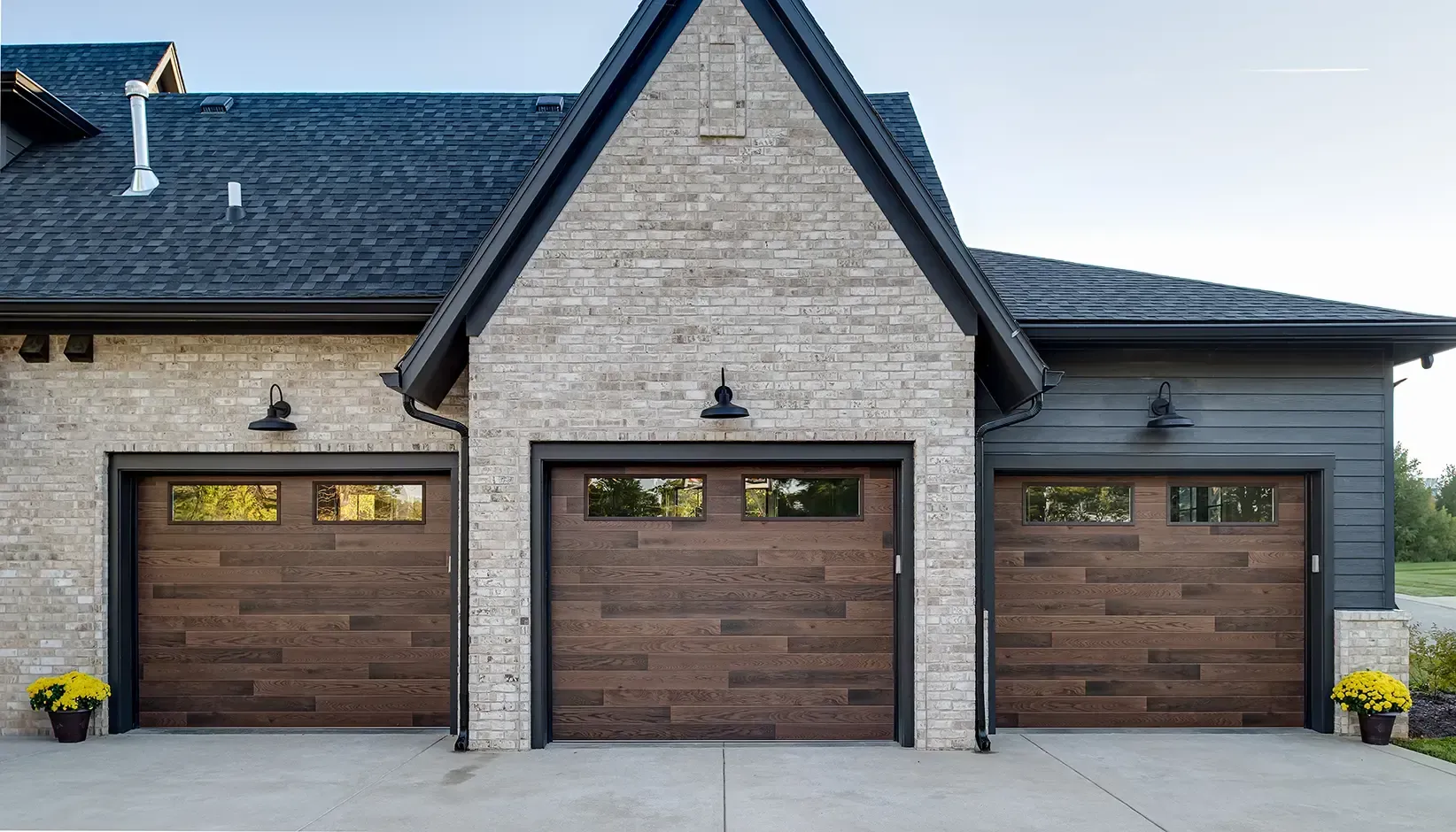 Modern house exterior with three brown garage doors and gray brick facade Modern house exterior with three brown garage doors and gray brick facade