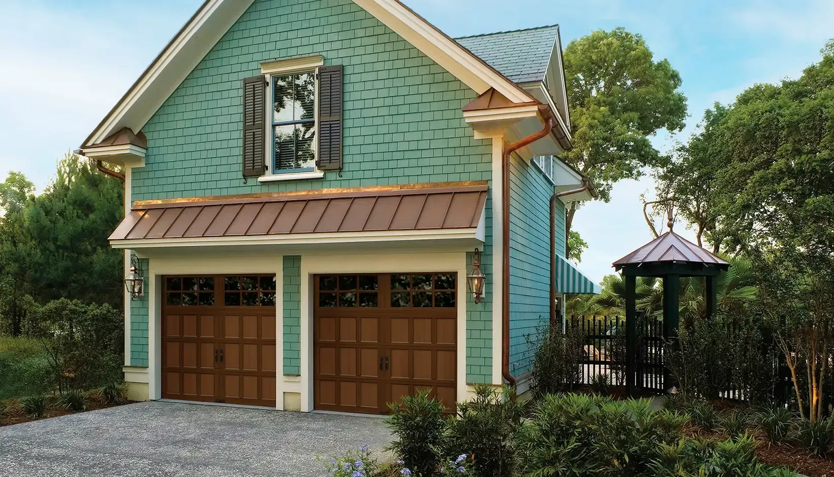 Blue cottage-style garage with two wooden doors, gravel driveway, and trees around it