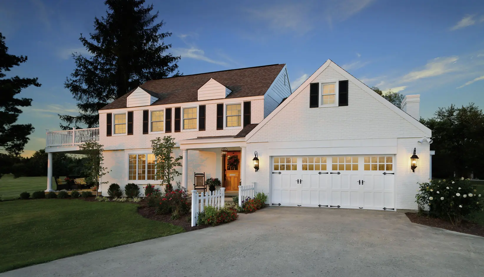 Suburban two-story house with white siding, attached garage, and a driveway at dusk