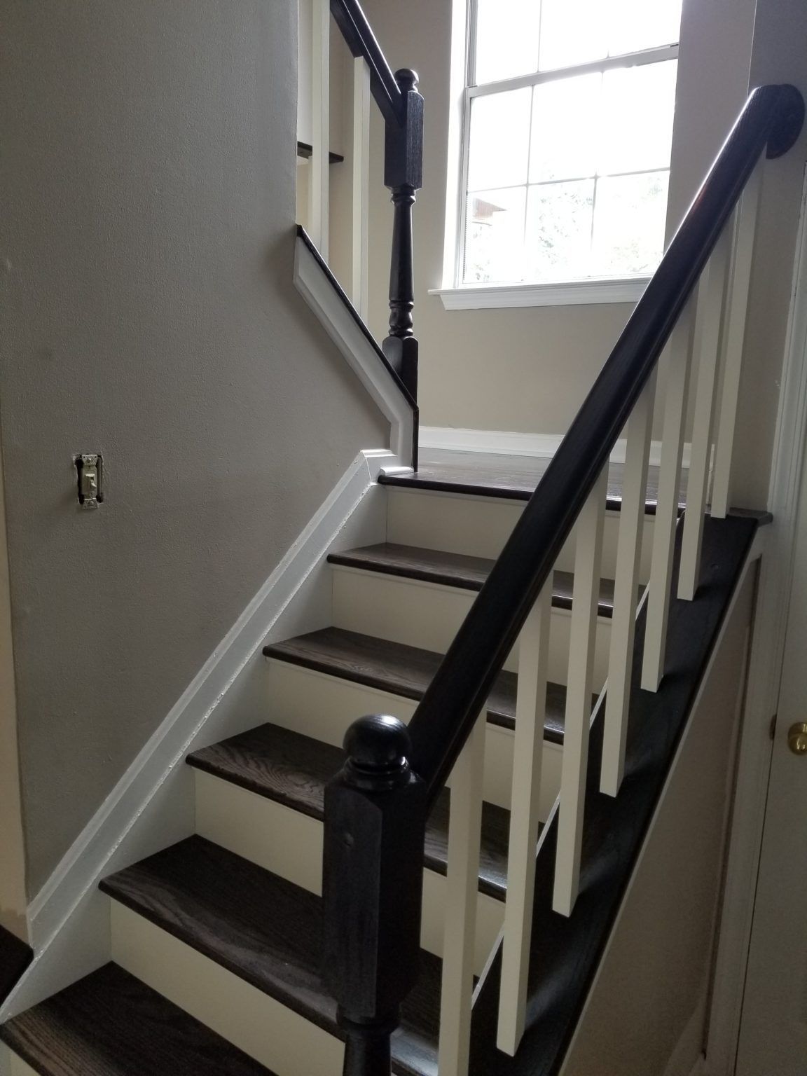 Staircase with black railing and white balusters. Dark wood-look steps and a window at the top.