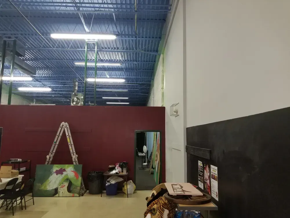 Interior view of a spacious warehouse with a high, blue ceiling and a burgundy wall, various objects are present.