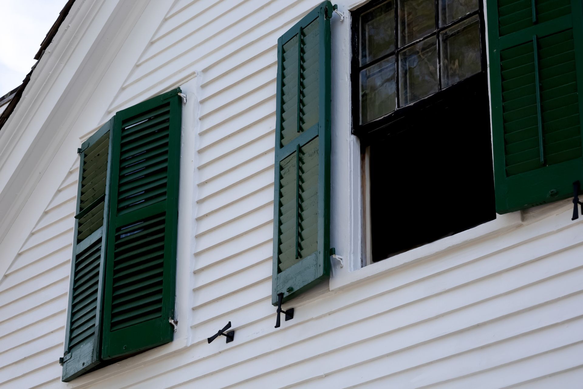 Person in a blue shirt and hat installing a dark gutter on a white wall.