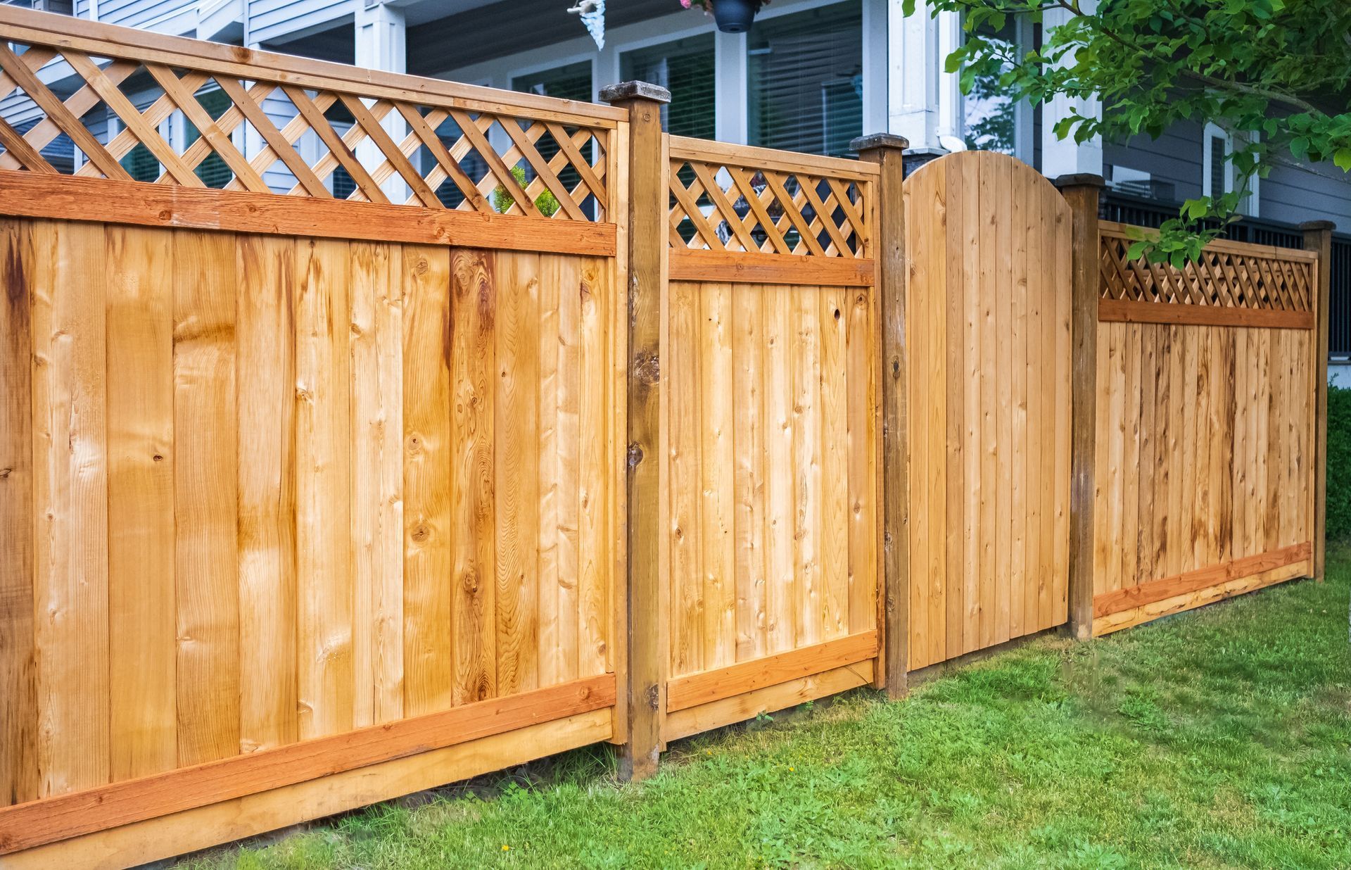 A brown metal fence with brick pillars and a gate in front of a house.