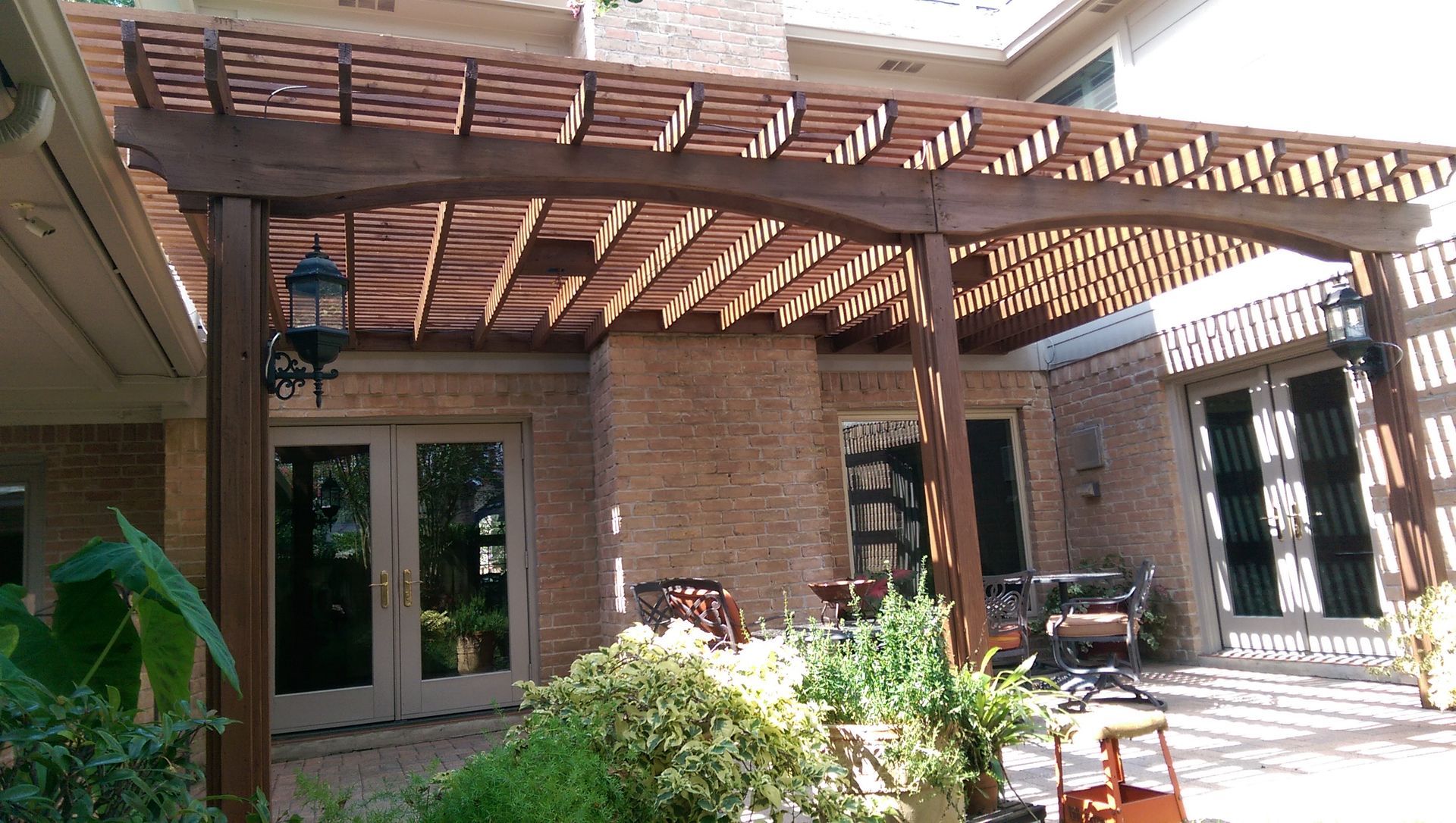 Patio with a pool, water view, and fire pit. Wooden ceiling, screened enclosure, and sunny skies. Two wooden lounge chairs and footrests on a stone patio, with a stone wall and foliage in the background.