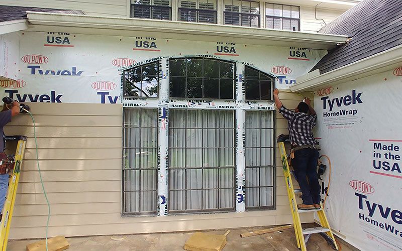 Man inspecting siding, touching it with his hand while holding a clipboard outside.