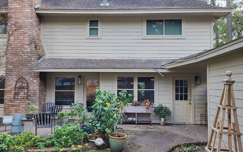 Beige house exterior with brick chimney, windows, and potted plants. Beige house exterior with brick chimney, windows, and potted plants.