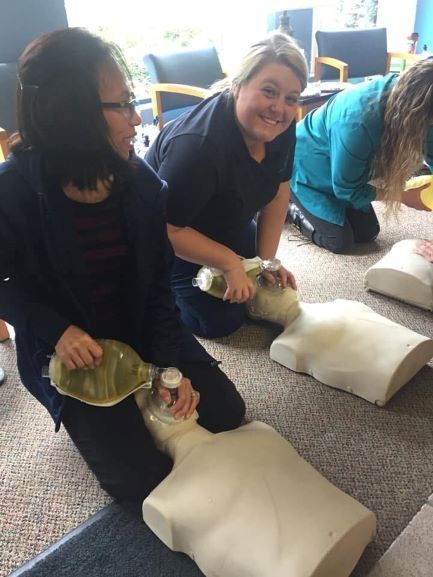 Two women are kneeling on the floor with a mannequin in front of them.