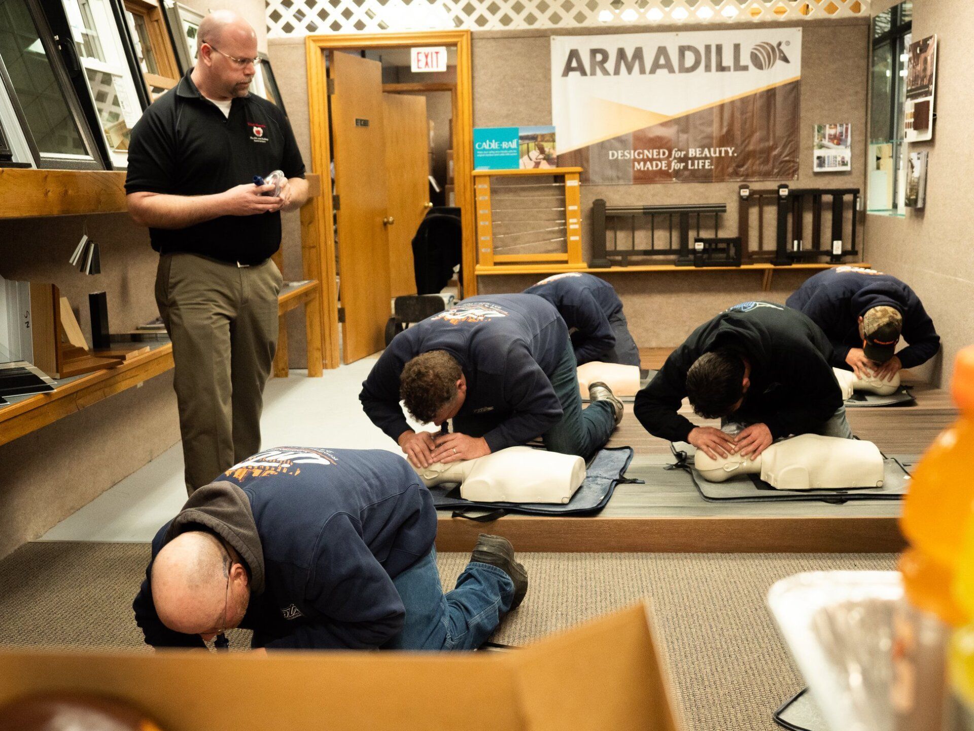 A group of men are practicing first aid in a room with a sign that says armadillo on it.