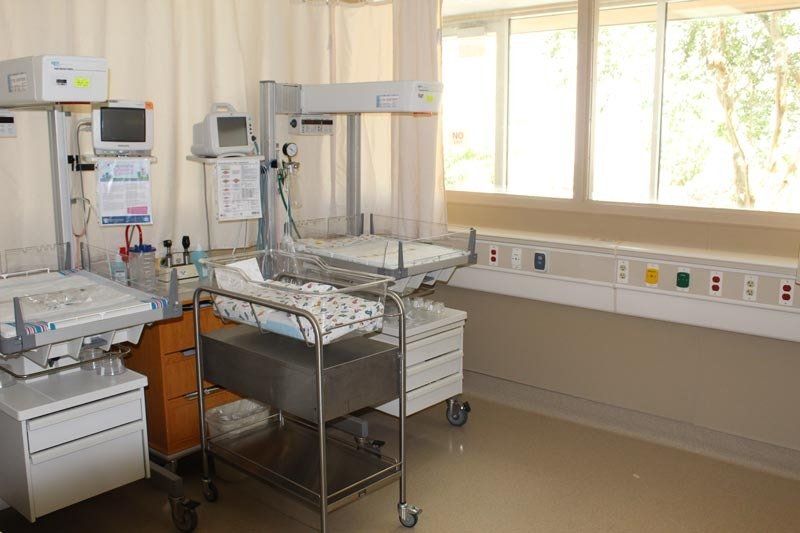 A hospital room with a baby in a crib and a window.