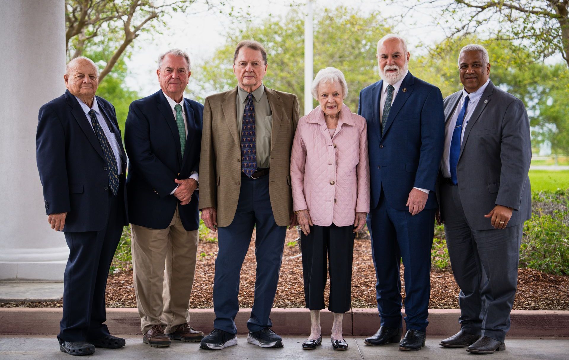 Photo of 5 men in suits and 1 lady in a pink blazer standing outside of the hospital