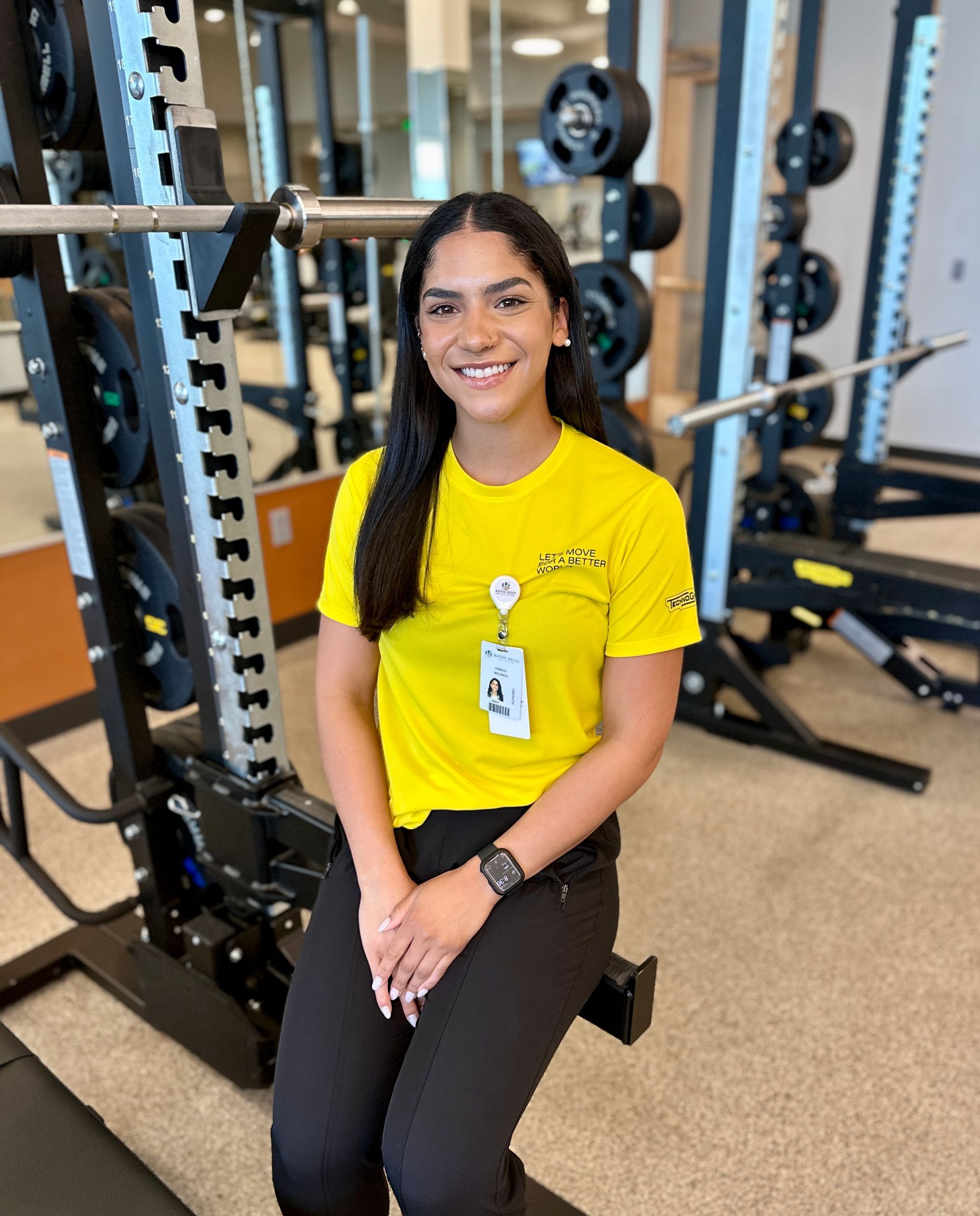 A woman in a yellow shirt is sitting on a bench in a gym.