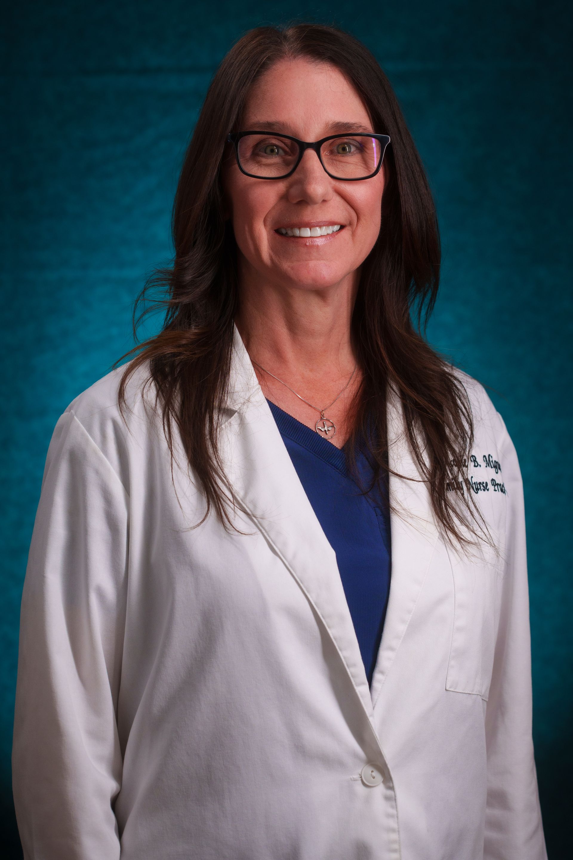 A woman in a white lab coat and glasses is smiling for the camera.