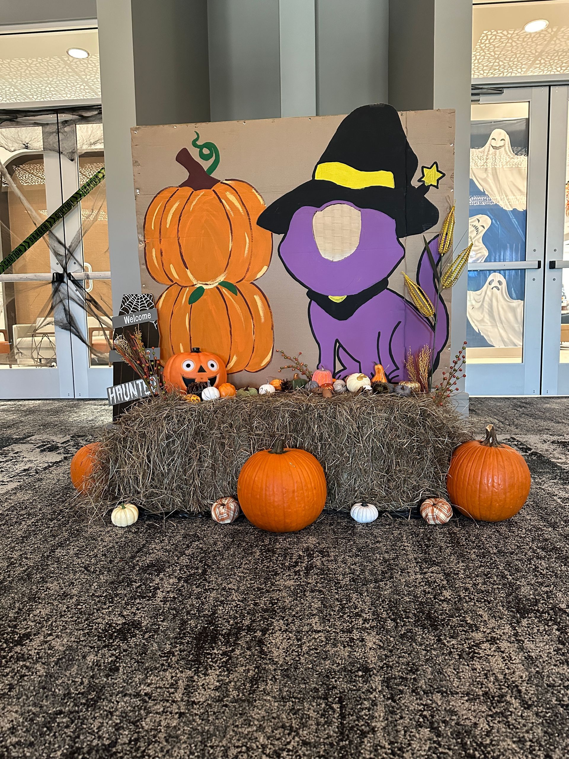 A purple dinosaur wearing a witch hat is surrounded by pumpkins and hay bales.