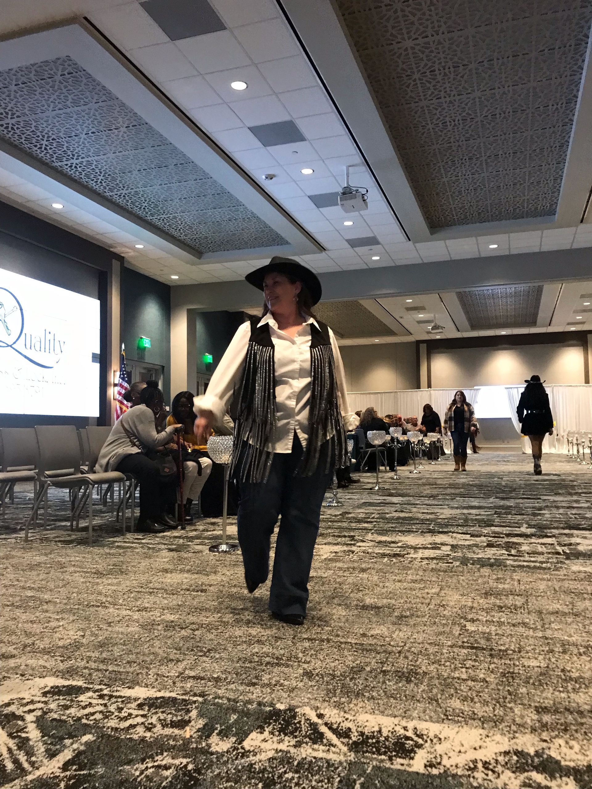 A woman in a cowboy hat is walking through a large room.