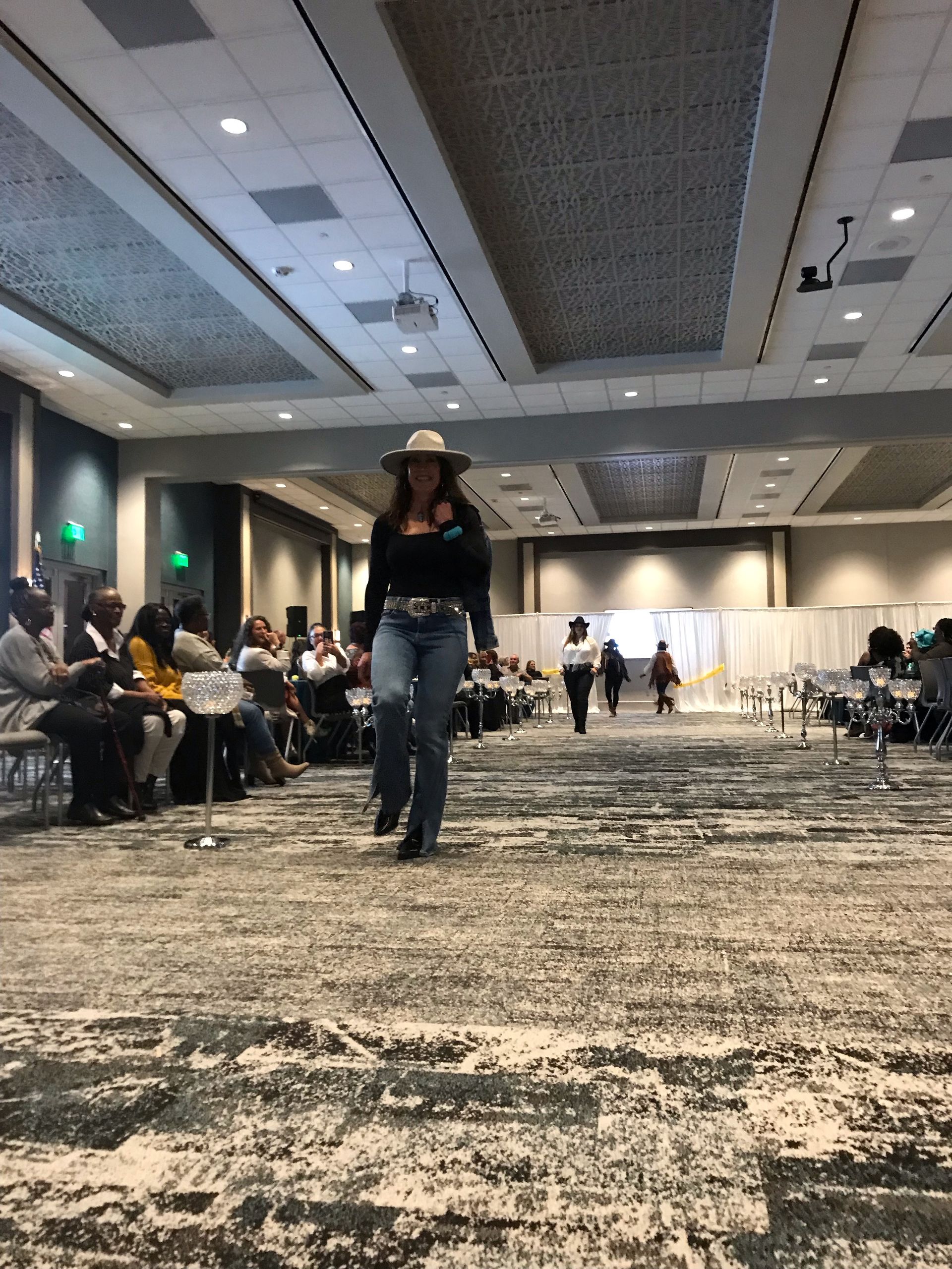 A woman in a cowboy hat is walking down a carpeted hallway.