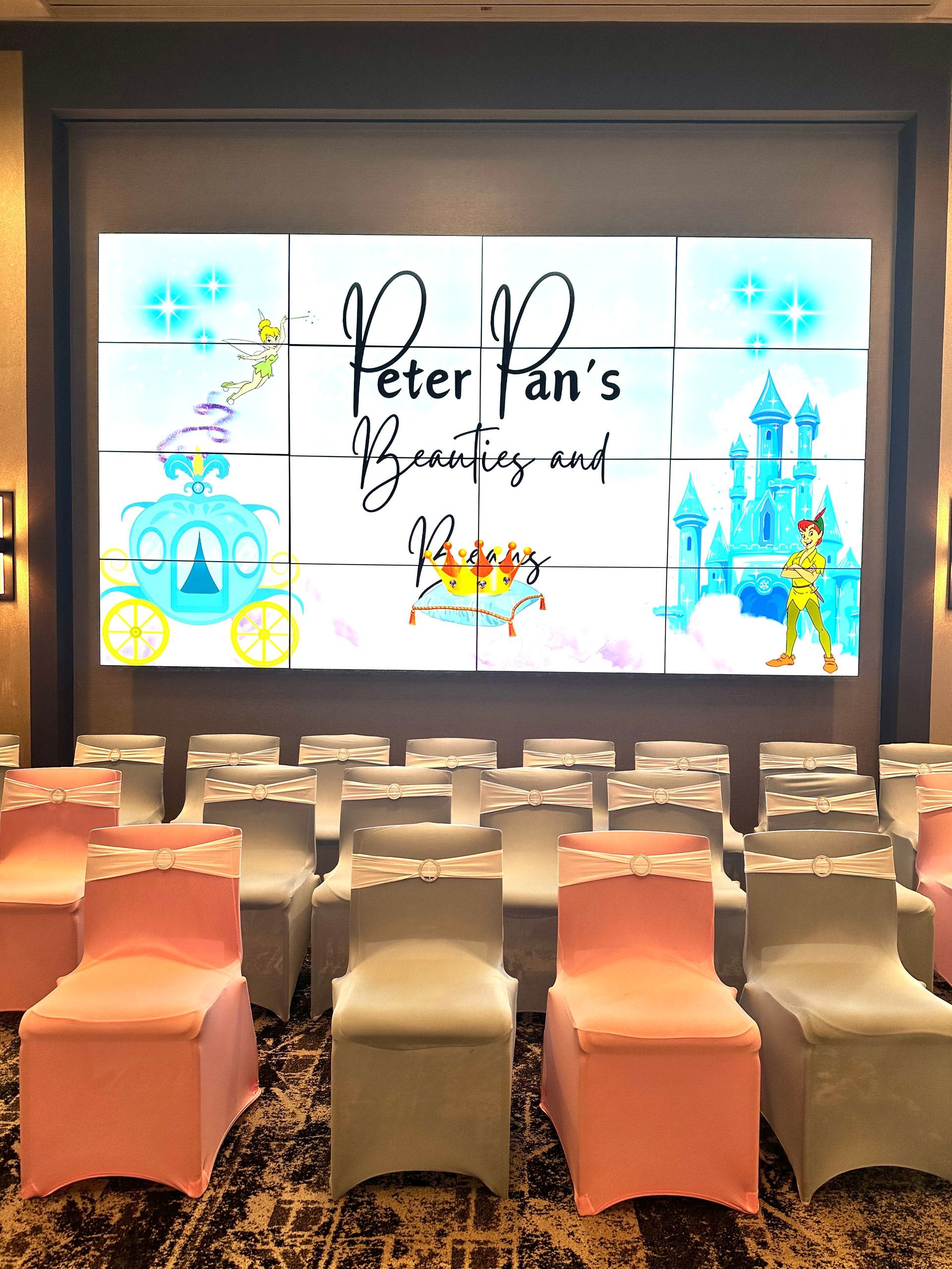 A room with pink chairs and a large screen that says peter pan 's