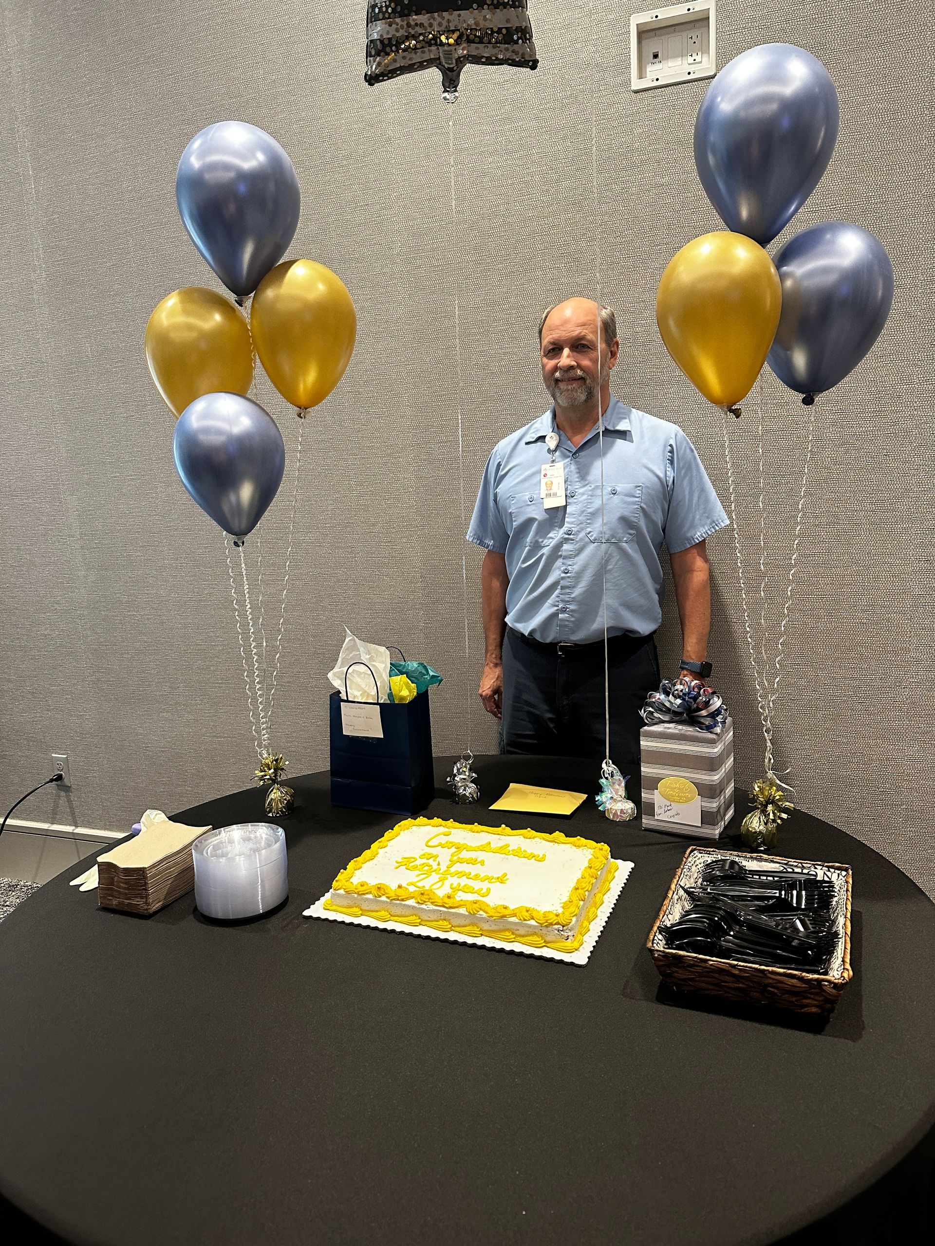A man is standing in front of a table with balloons and a cake.