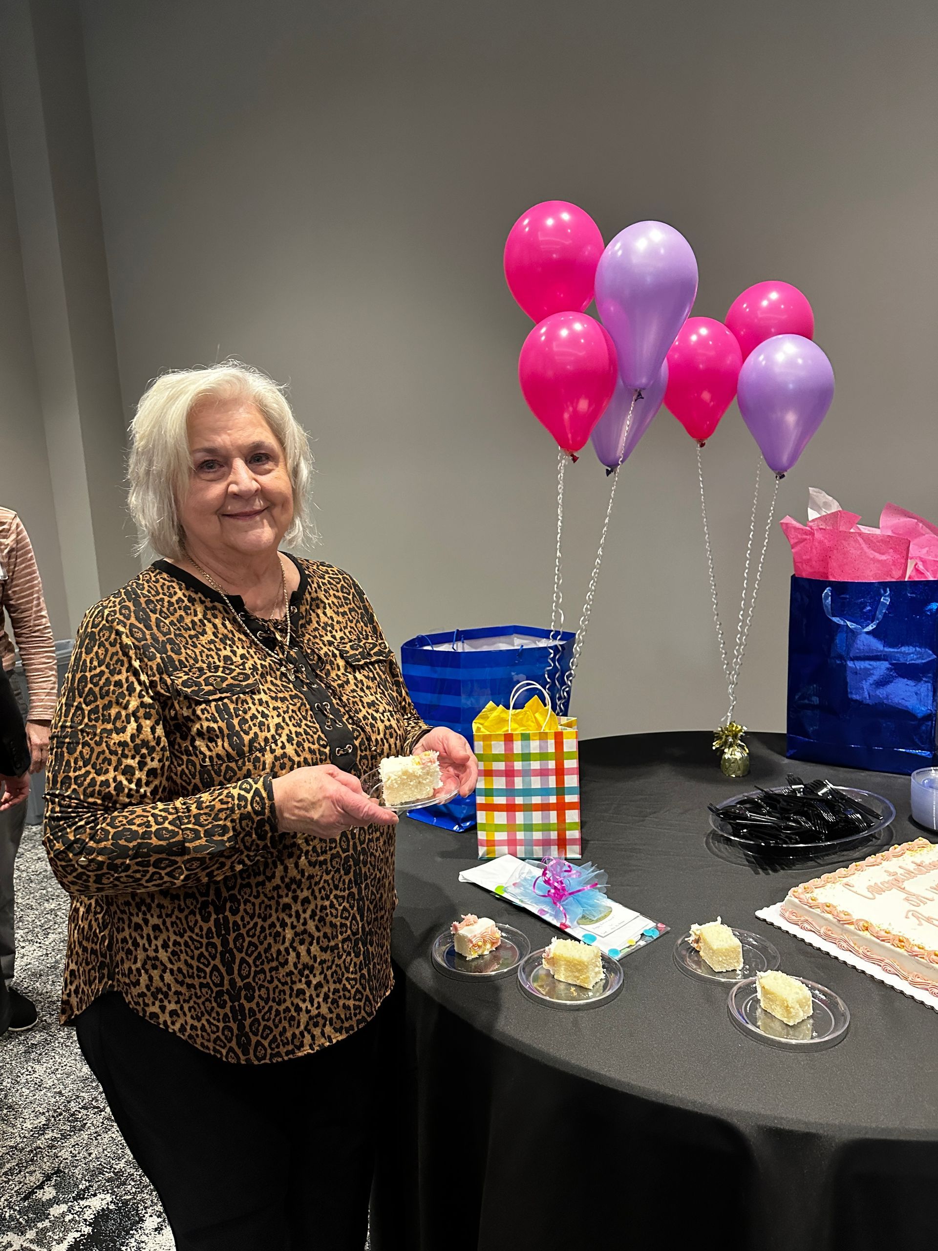 A woman is standing in front of a table with balloons and cake.