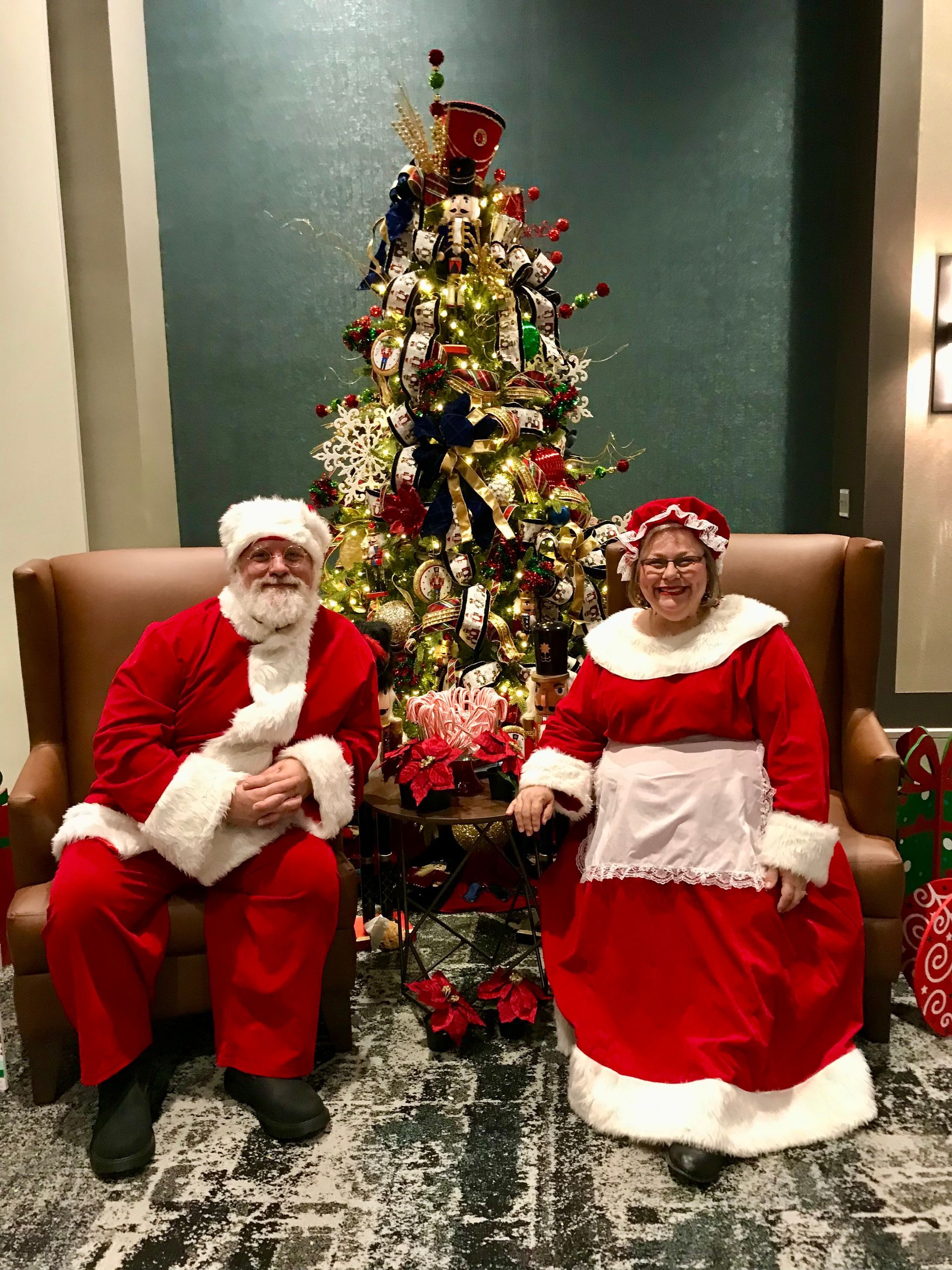 A man and a woman dressed as santa claus are sitting in front of a christmas tree.