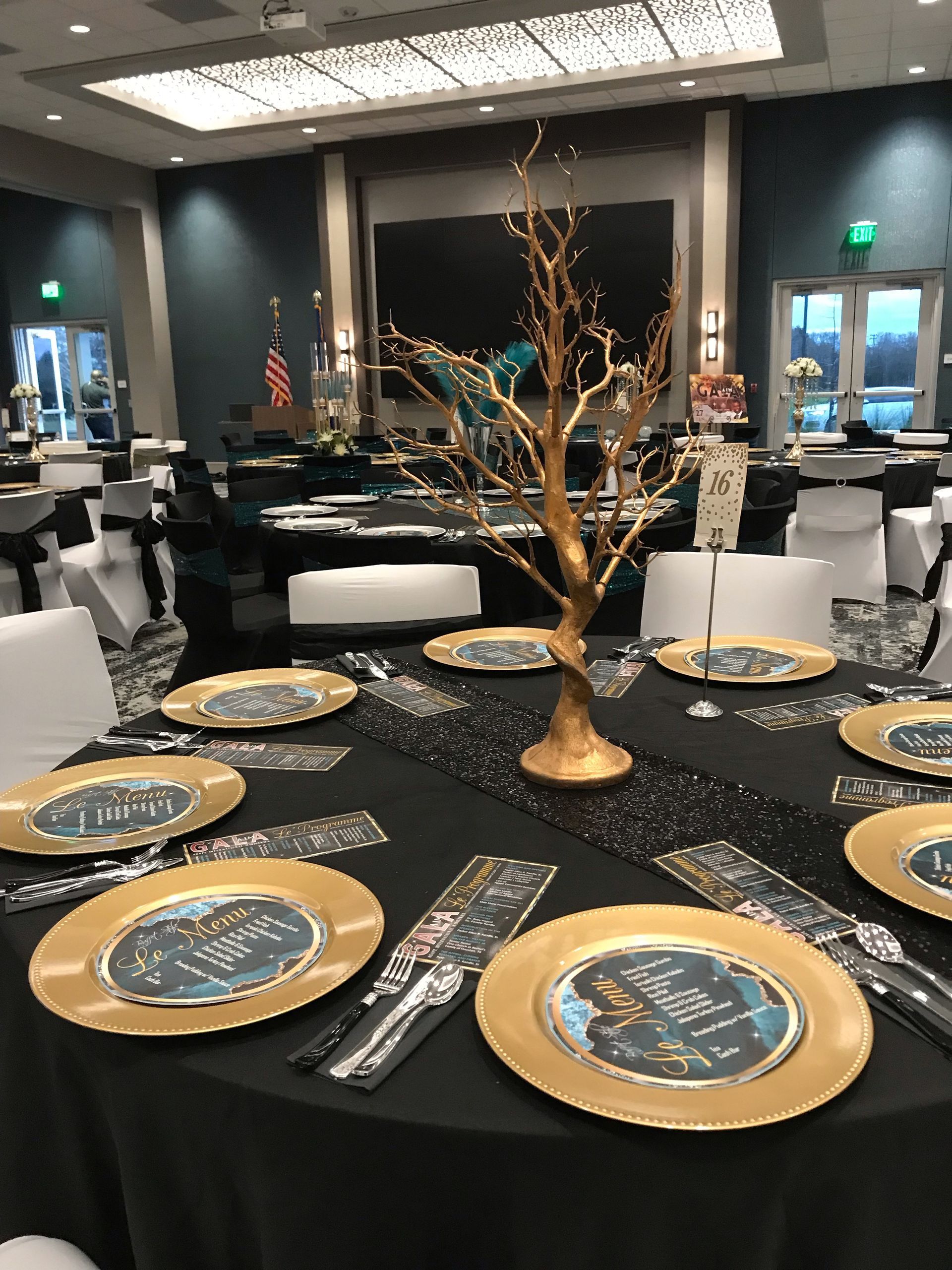 A table set for a party with gold plates and a gold tree centerpiece.