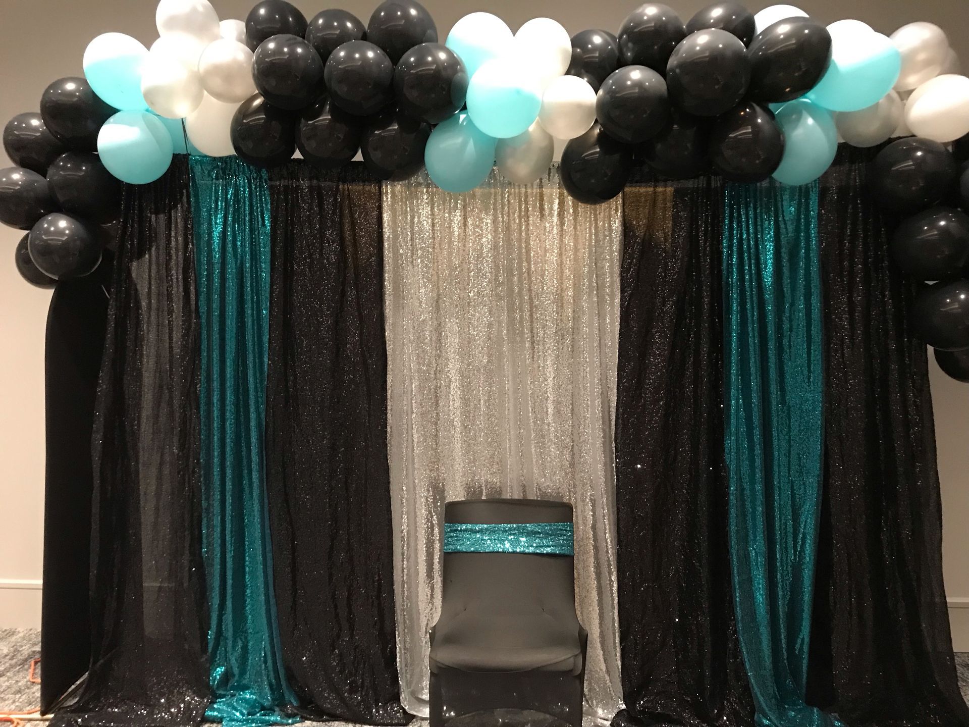 A chair is sitting in front of a black and blue backdrop with balloons.