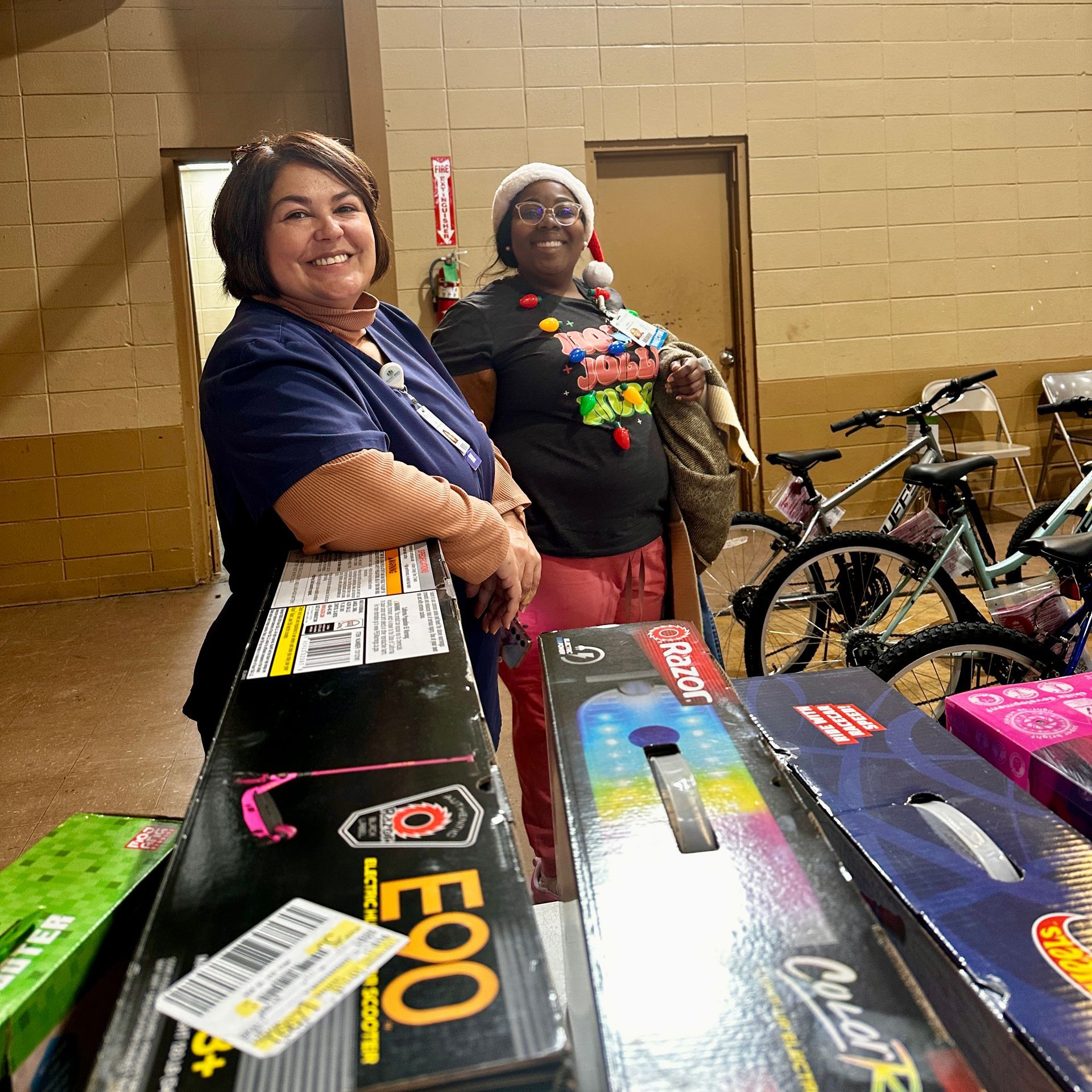 2 women standing next to bicycles and a table of toys