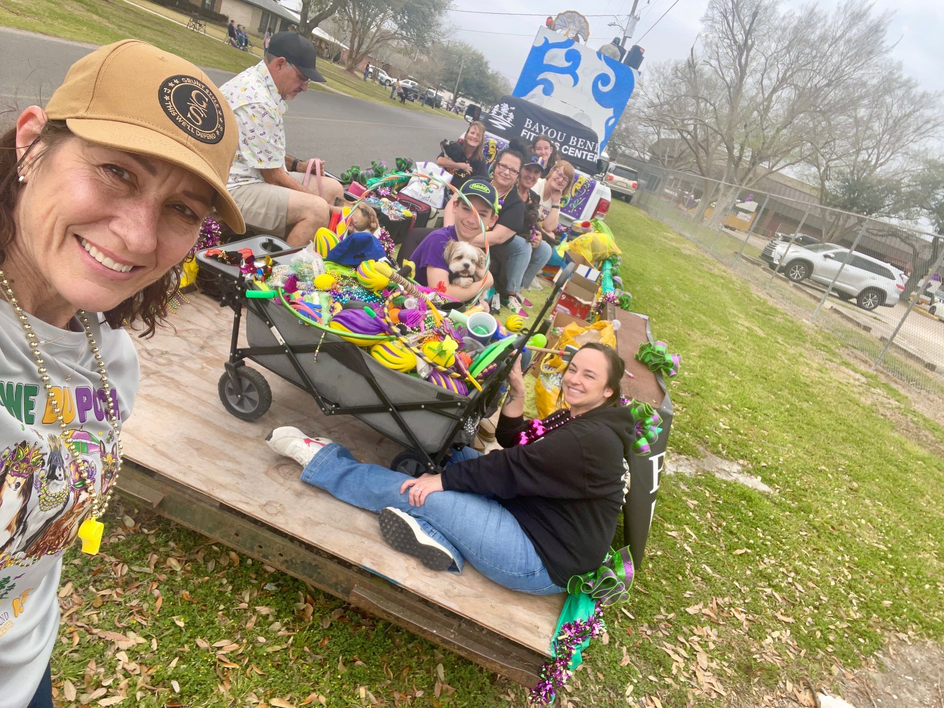 Woman in tan ball cap standing in front of a mardi gras float containing people and dogs