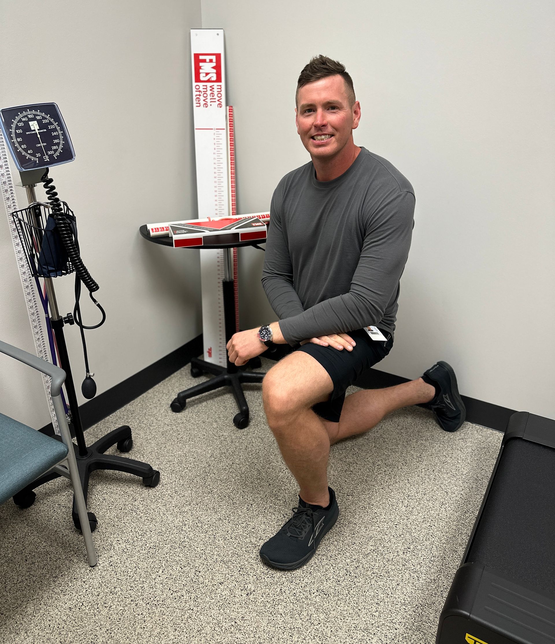 A man is kneeling down in a room next to a treadmill.