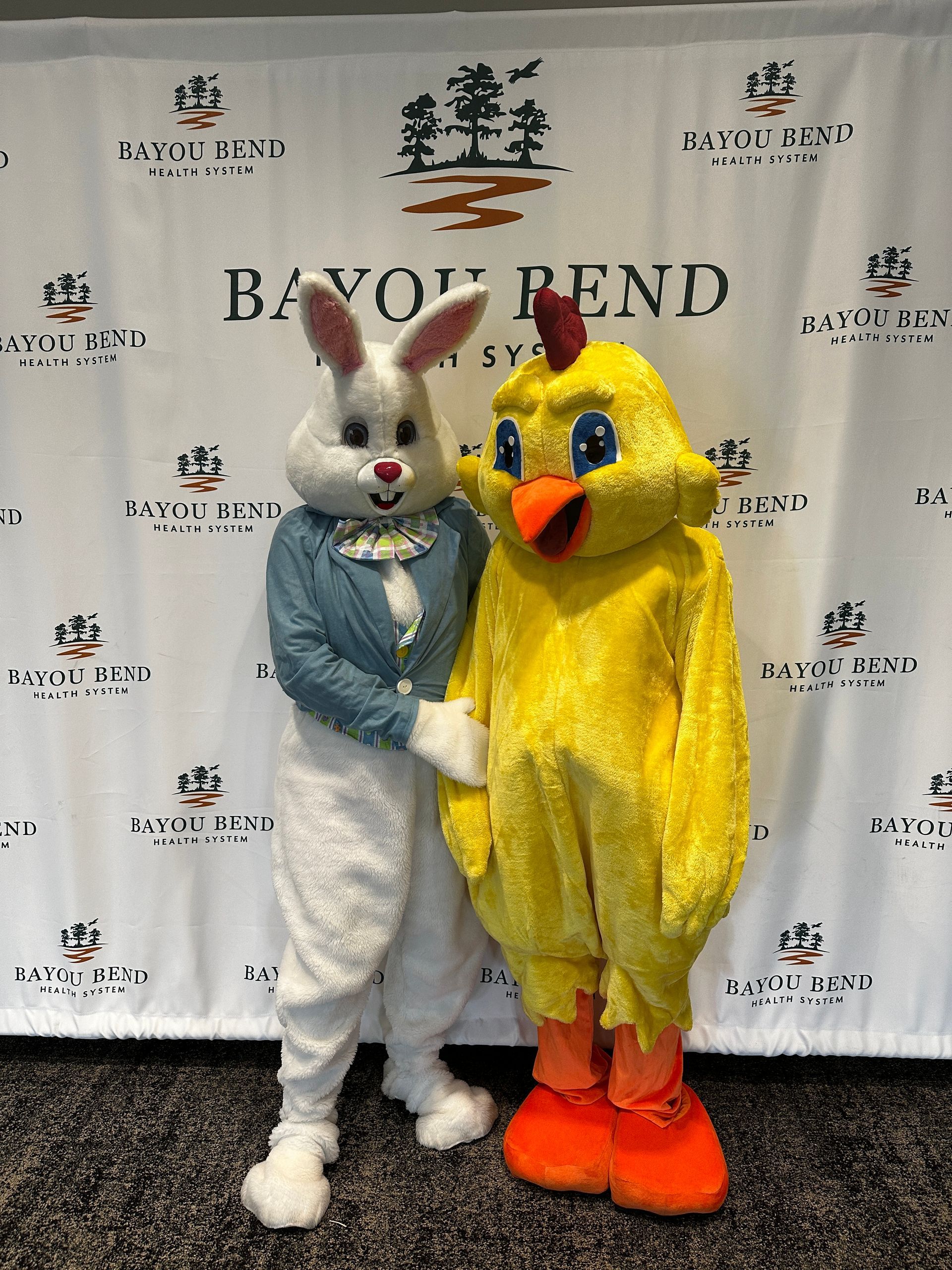 People in Easter Bunny and chick costumes standing in front of a backdrop that reads 