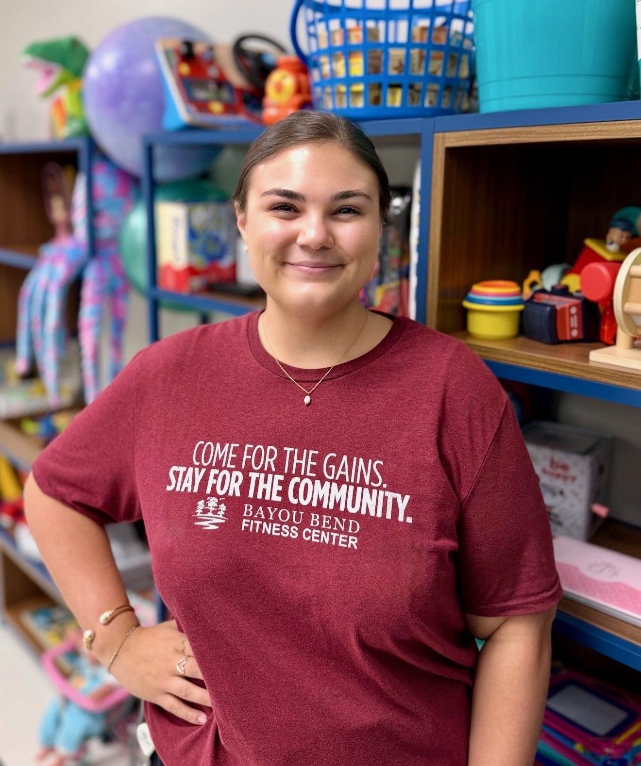 A woman in a blue shirt is standing in front of a shelf full of toys.