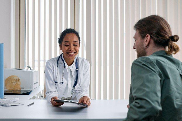 A doctor is sitting at a desk talking to a patient.