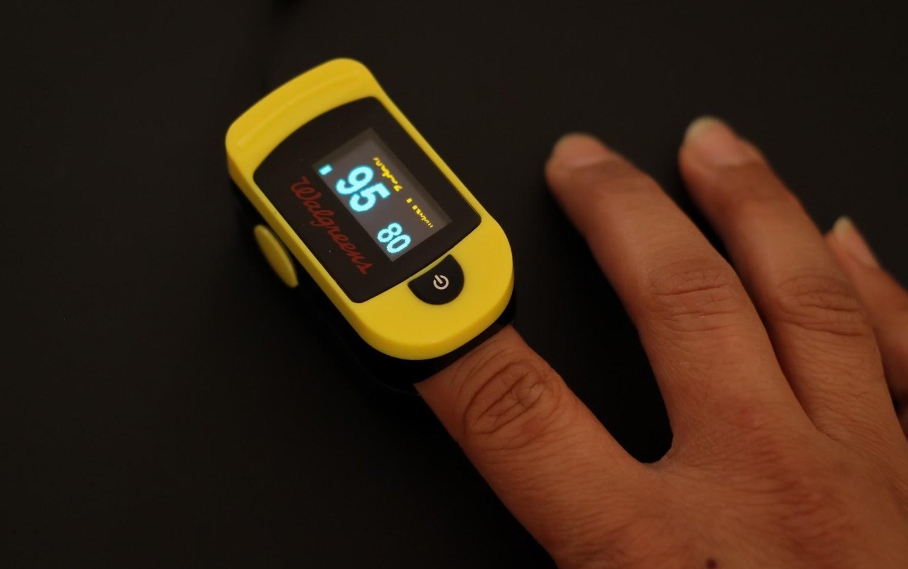 A person is using a yellow pulse oximeter on their finger