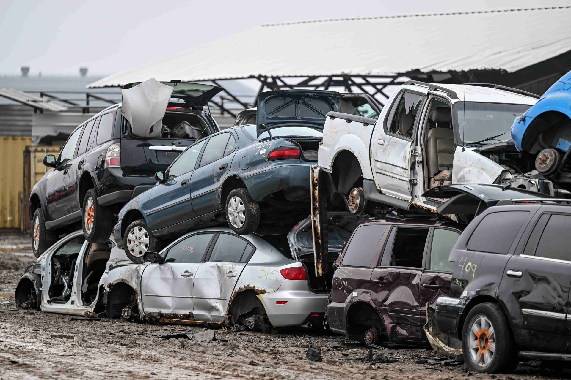 Pile of crushed cars at a salvage yard; rusted and stacked, overcast sky.