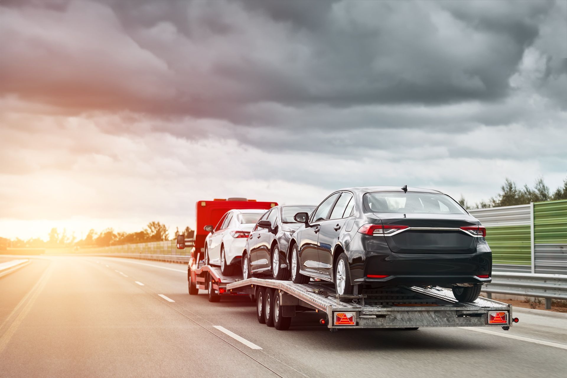 Cars on a car carrier truck driving on a highway, under a cloudy sky.