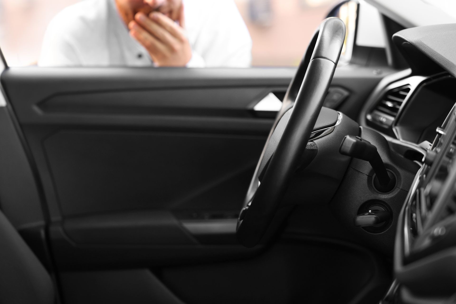Man looking into car; door open; steering wheel in foreground.