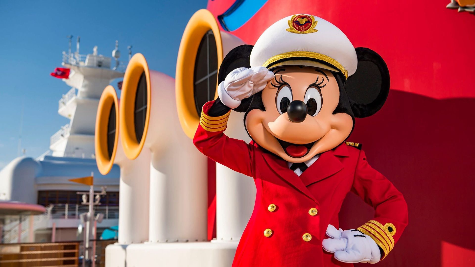 Mickey Mouse in a red captain’s coat salutes aboard a white ship with bright red and yellow funnels.
