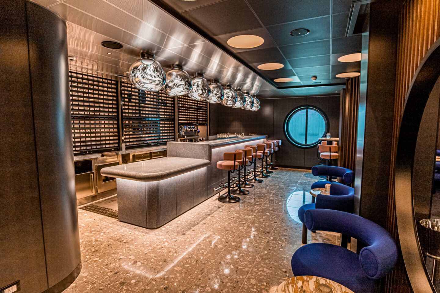 Modern lounge bar with curved blue chairs, a long counter, and warm ambient lighting